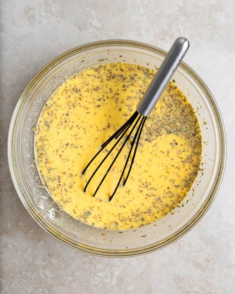 Whisked egg, ricotta, milk, and spices in a bowl.
