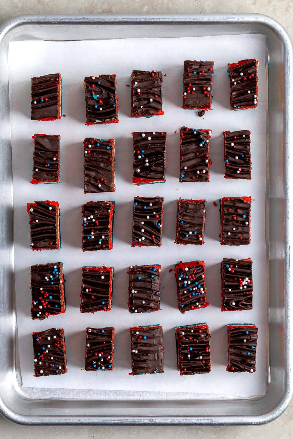Rows of lined up red white and blue rainbow cookies on a sheet pan.