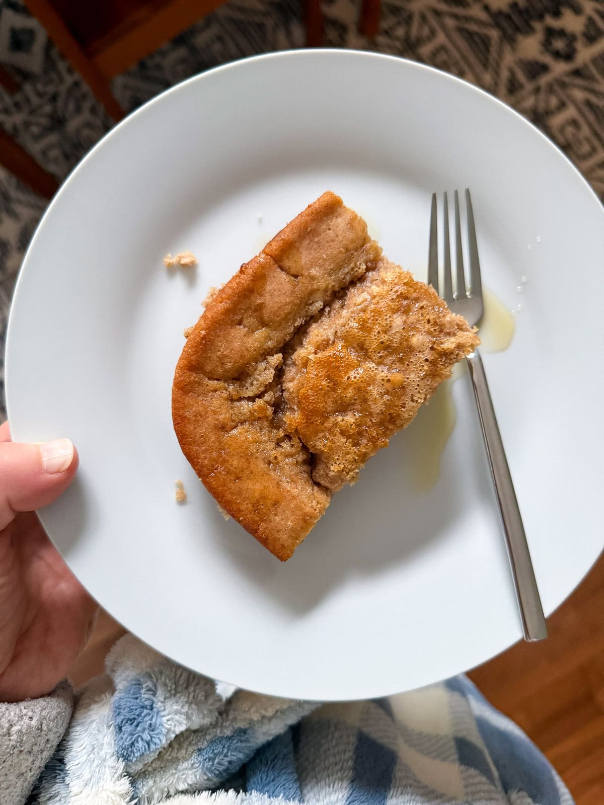 A corner wedge of a baked pancake on a plate drizzled with maple syrup.