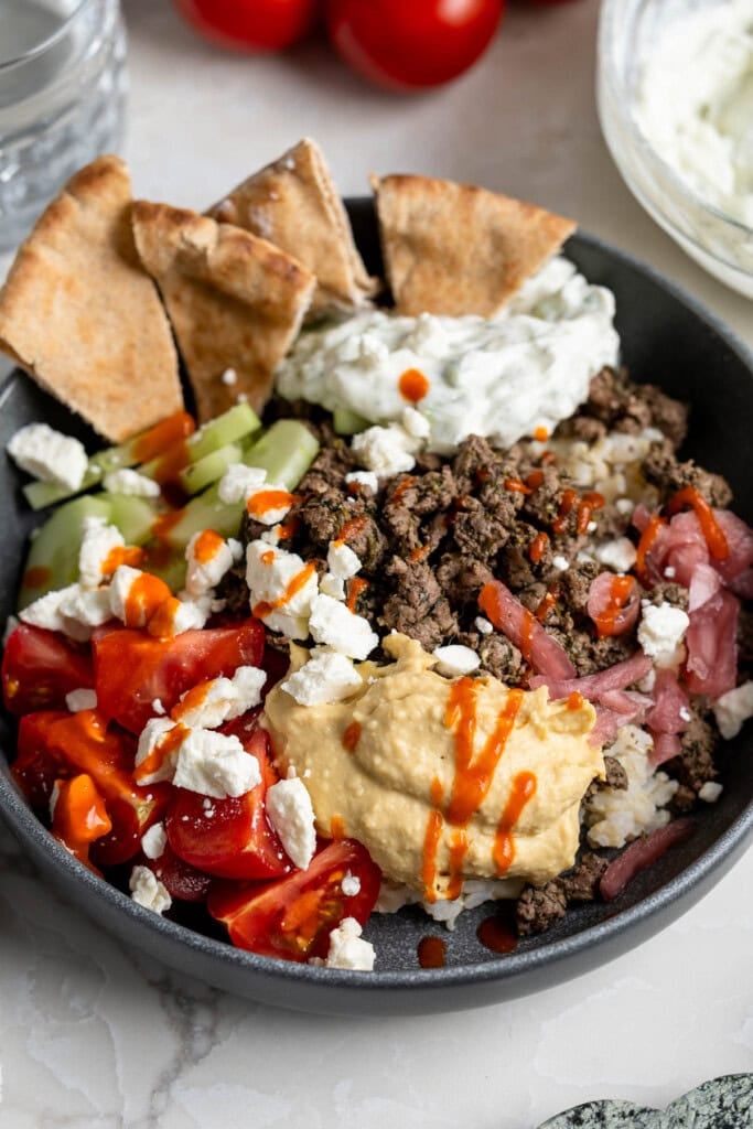 A Mediterranean beef rice bowl topped with hummus, tomatoes, feta, red onion, pita chips, etc.