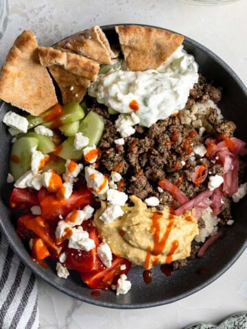 A bowl of dill spiced beef, hummus, brown rice, veggies, feta, and pita.