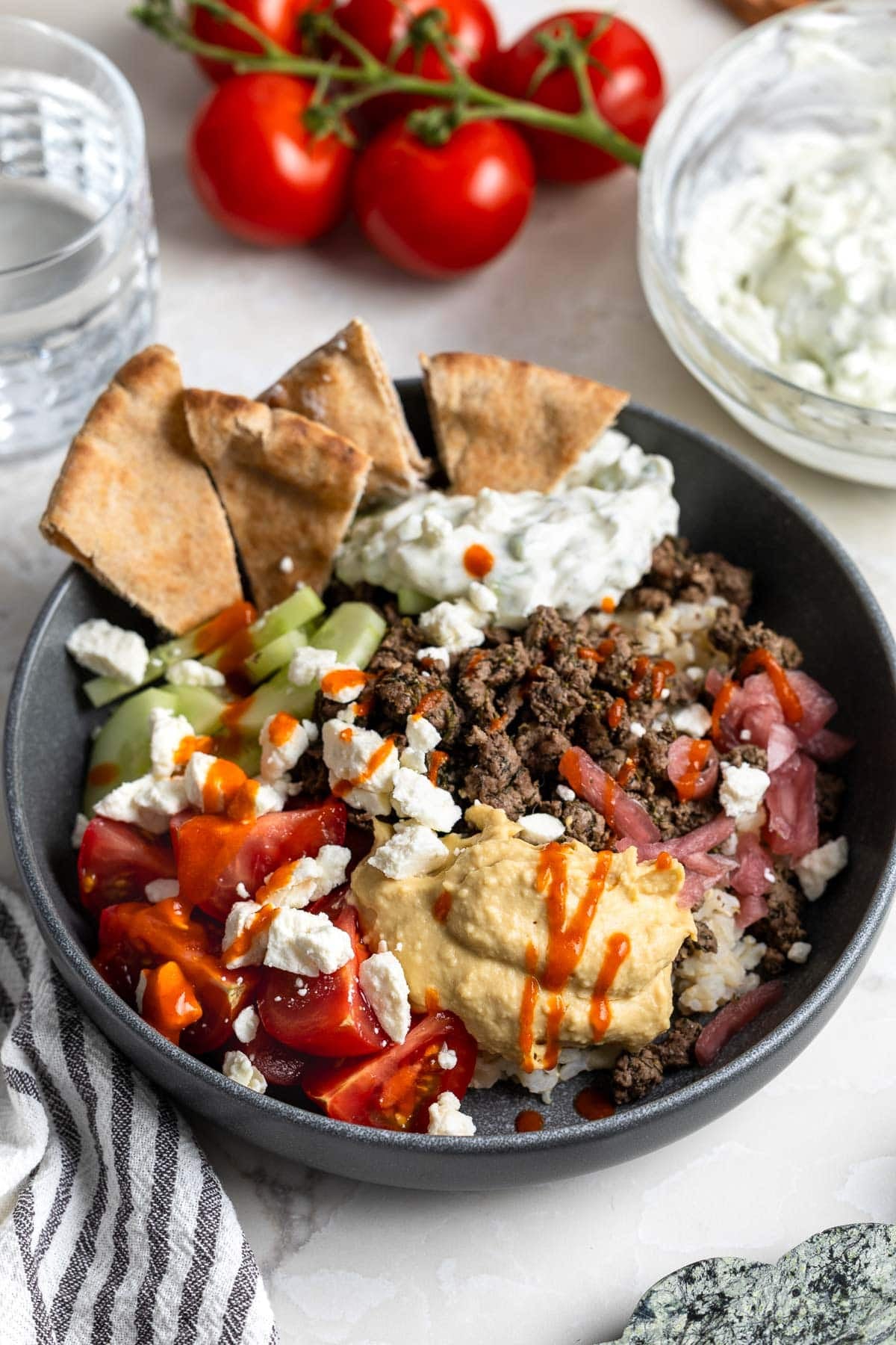 A Mediterranean beef rice bowl topped with hummus, tomatoes, feta, red onion, pita chips, etc.