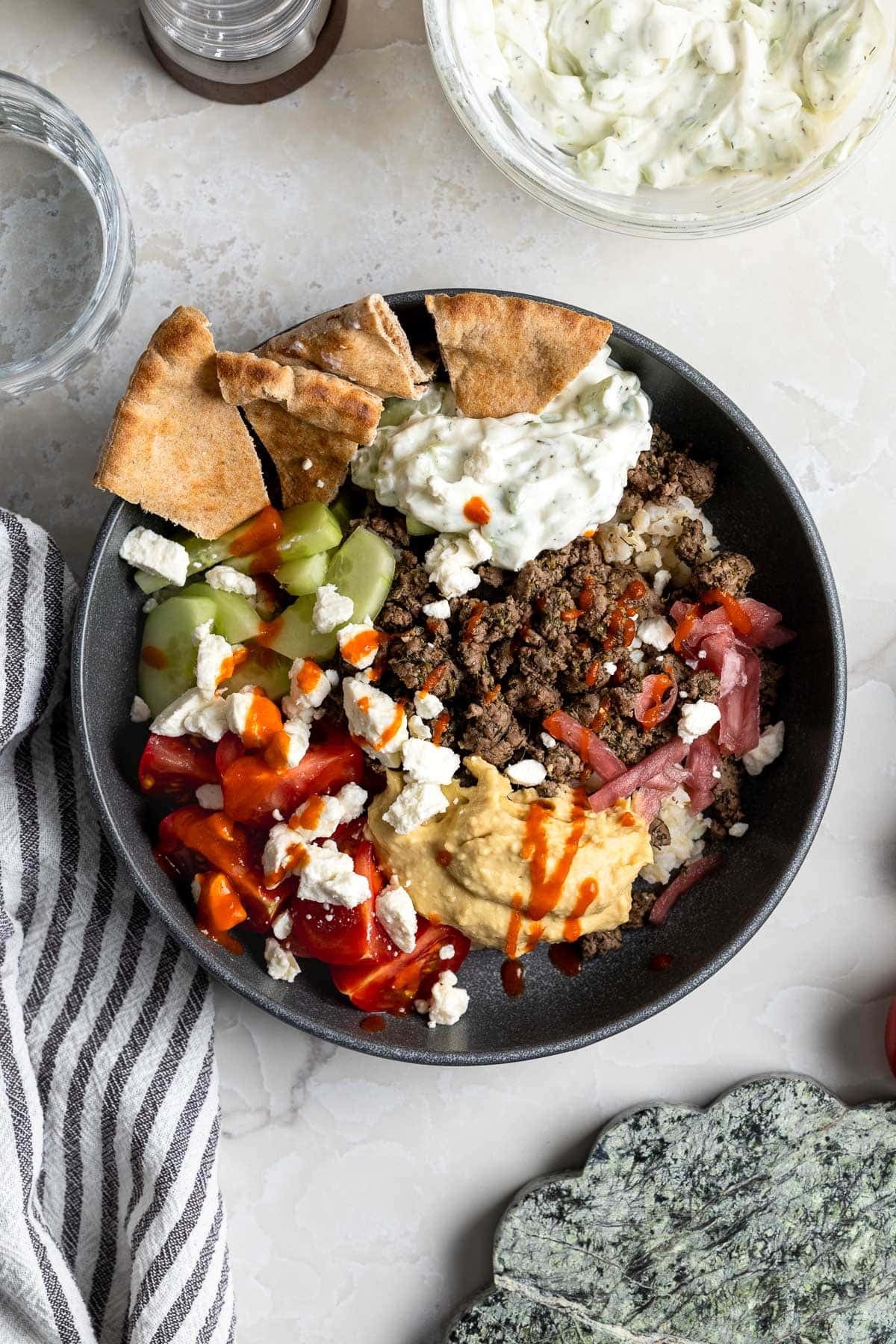 A bowl of dill spiced beef, hummus, brown rice, veggies, feta, and pita.