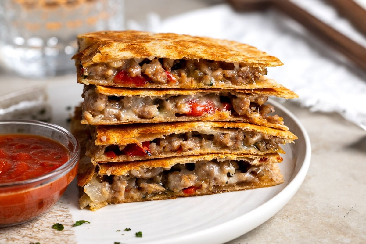Sausage quesadilla slices on a plate with marinara for dipping.