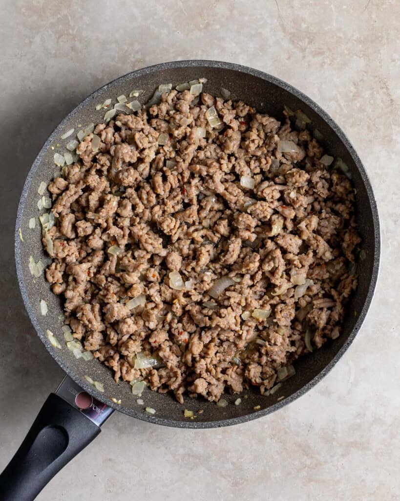 Cooked and crumbled Italian sausage, onion and garlic in a pan.