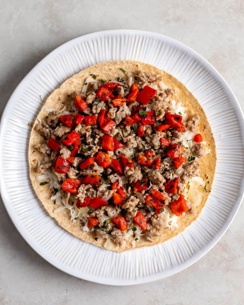 The Italian sausage, peppers, onions, and cheese layered onto a tortilla before placing the top tortilla on.