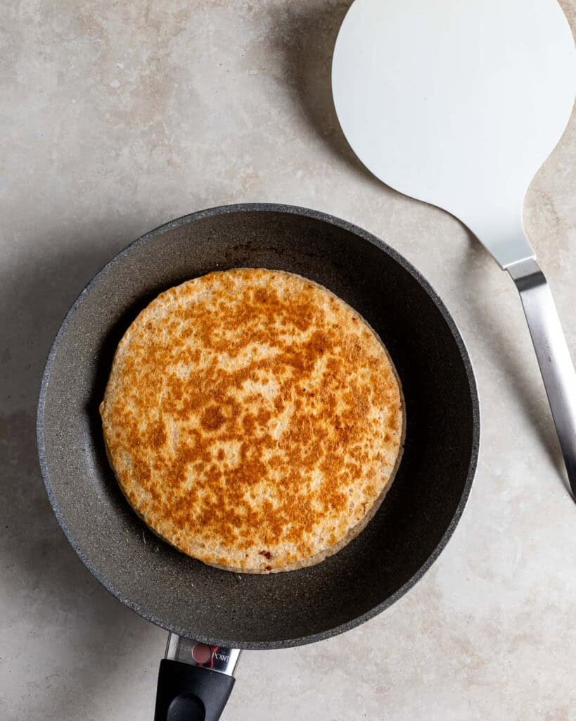 The golden-brown, crisp quesadilla in a pan next to a very large flipper spatula.