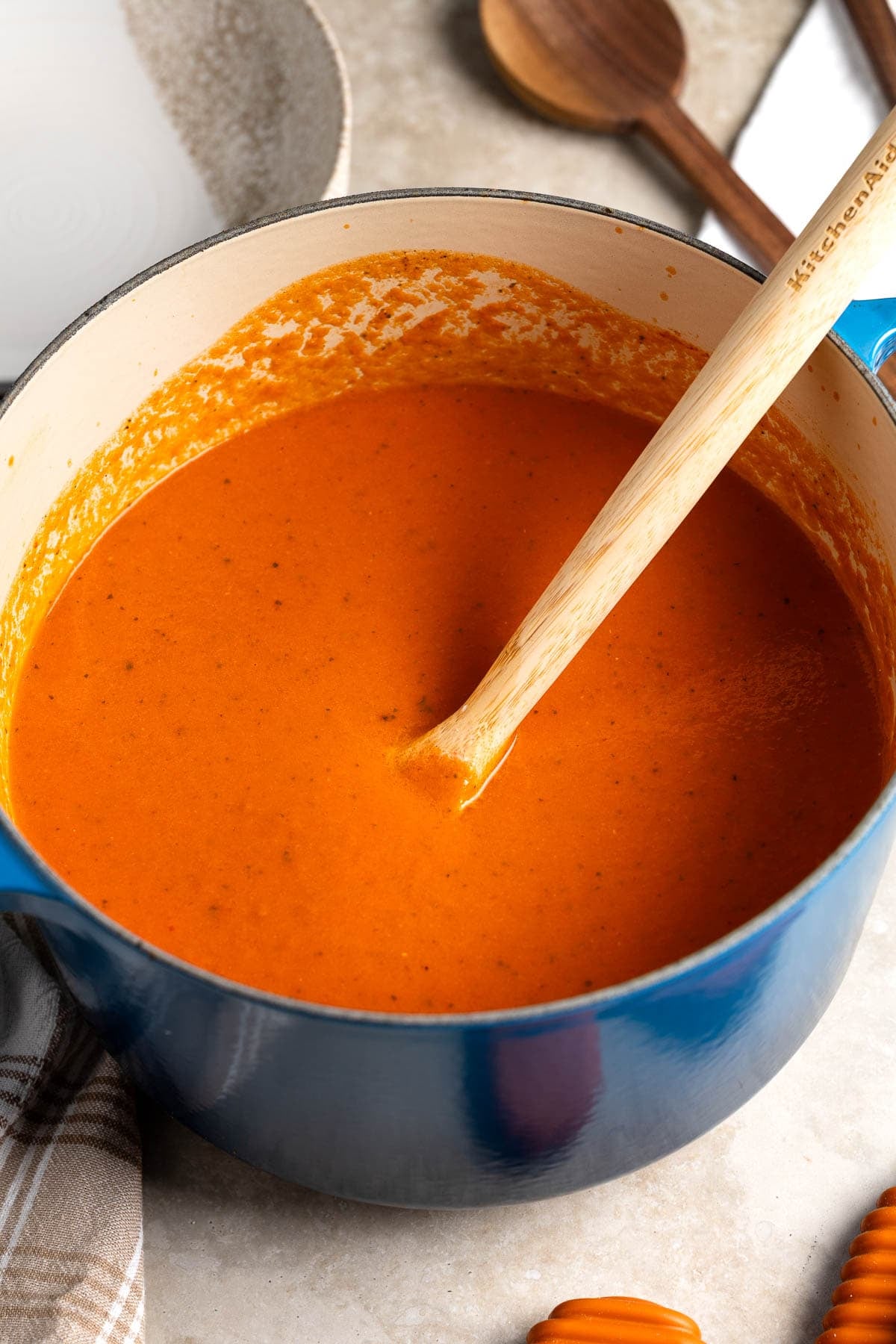 A big pot of tomato soup with a wooden spoon in it.