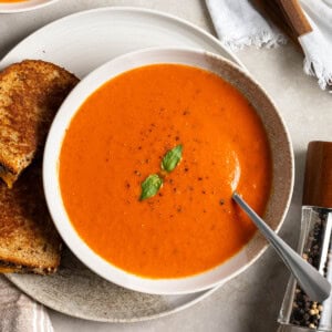A shallow bowl of tomato soup made with canned tomatoes on a plate with a grilled cheese sandwich accompaniment.