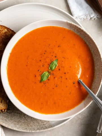 A shallow bowl of tomato soup made with canned tomatoes on a plate with a grilled cheese sandwich accompaniment.