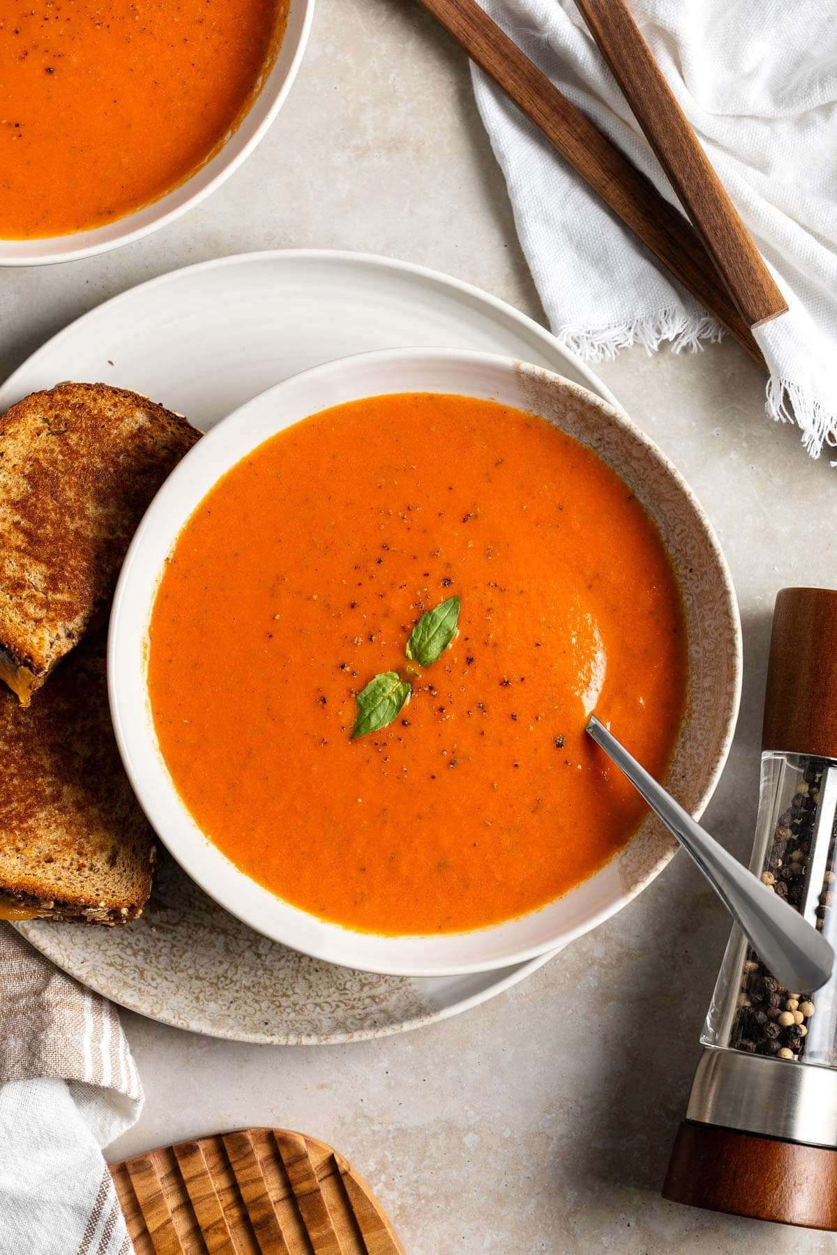 A shallow bowl of tomato soup made with canned tomatoes on a plate with a grilled cheese sandwich accompaniment.