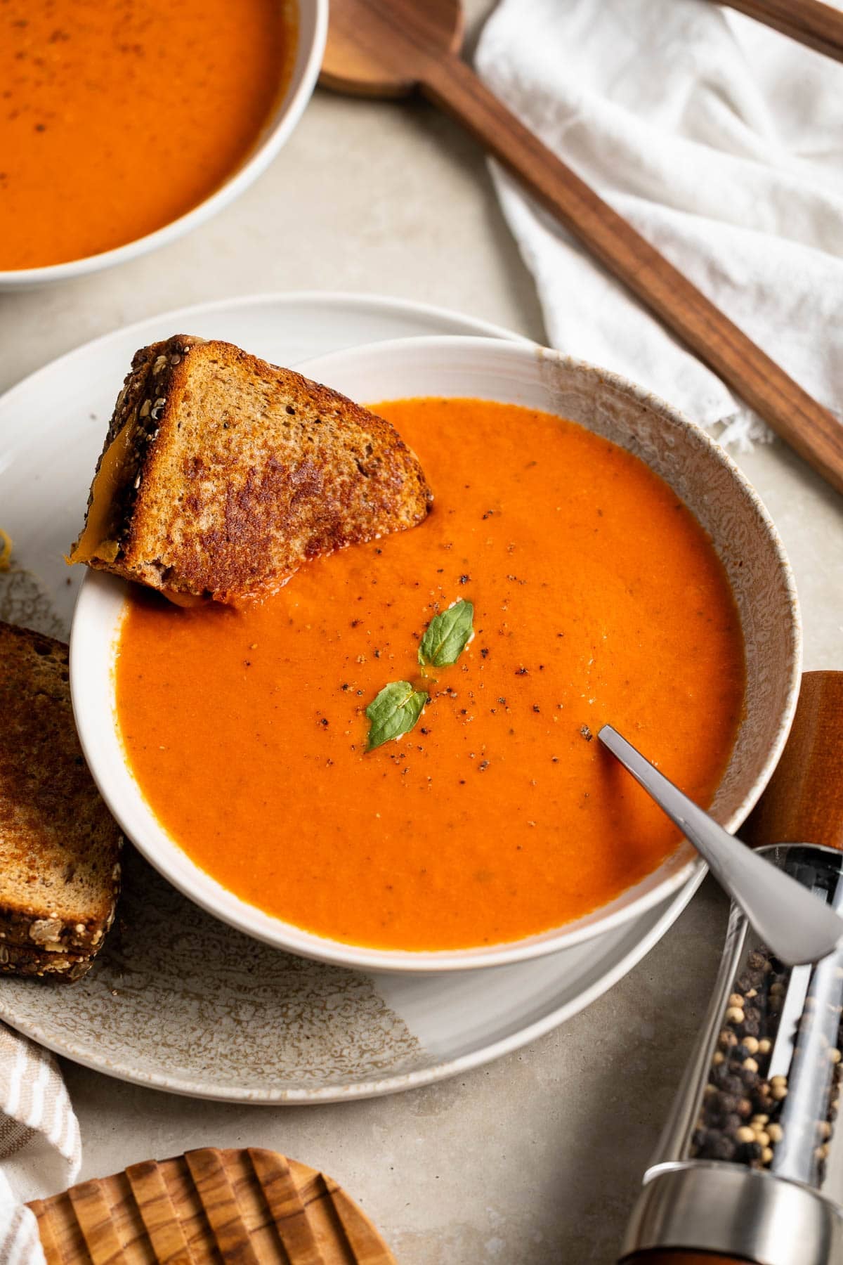Weeknight tomato soup in a shallow bowl garnished with basil with half of a grilled cheese sandwich dunked in.