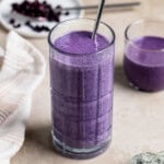 A wild blueberry smoothie in a tall glass with a metal straw and a short glass.