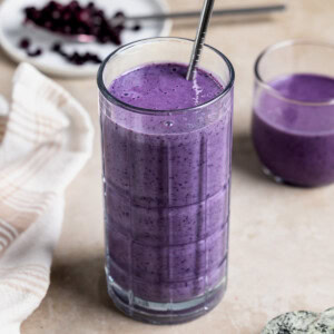 A wild blueberry smoothie in a tall glass with a metal straw and a short glass.