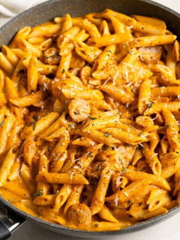 A pan of penne and chicken sausage coated in a creamy pumpkin pasta sauce.