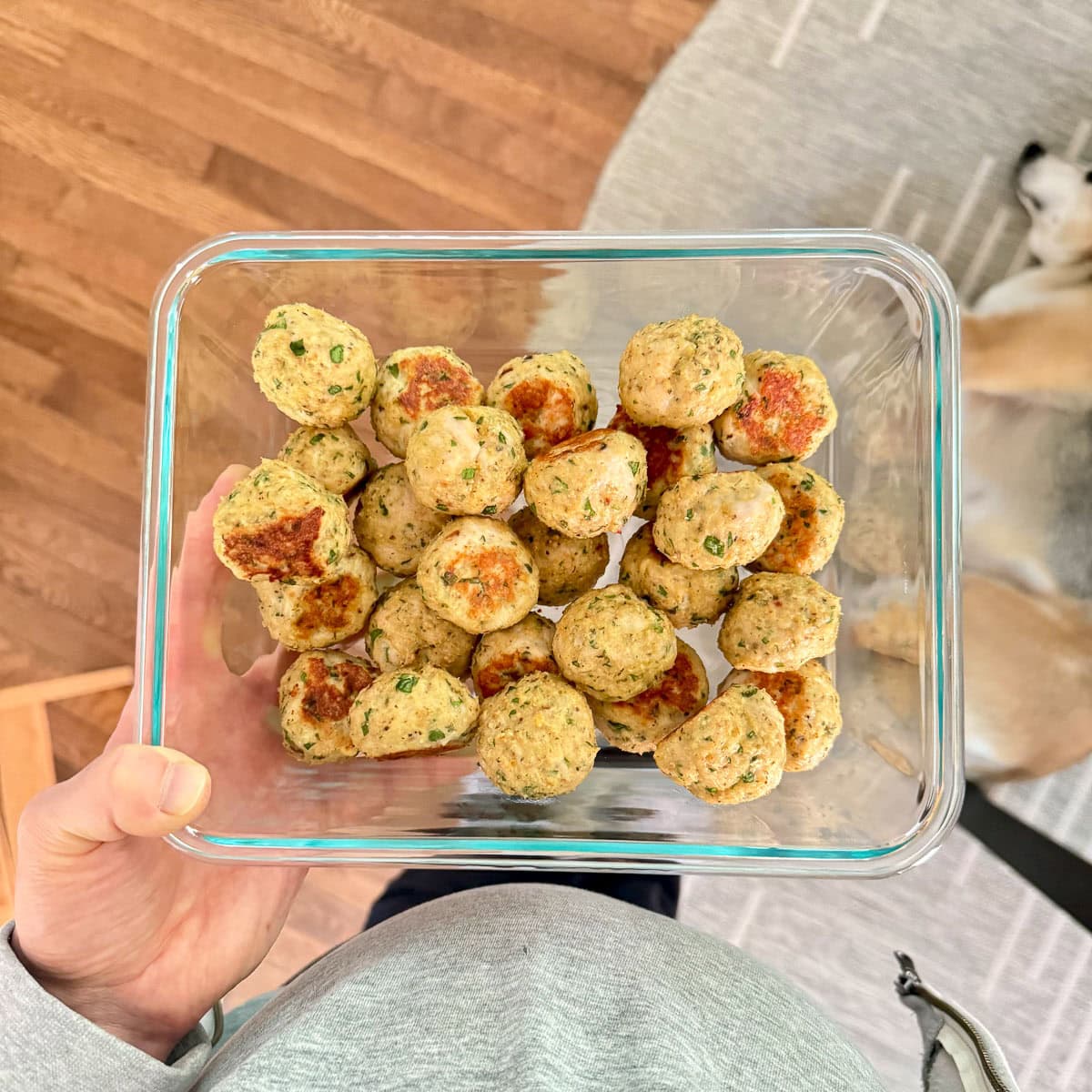 A woman holding a glass storage container of baked turkey meatballs.
