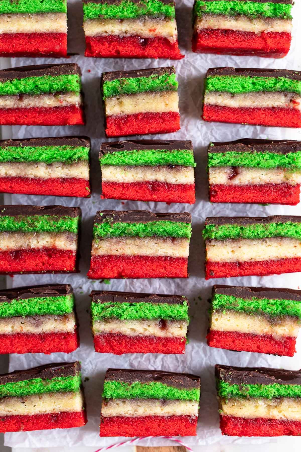 A side view of a batch of chocolate-topped green, white, and red rainbow cookies.