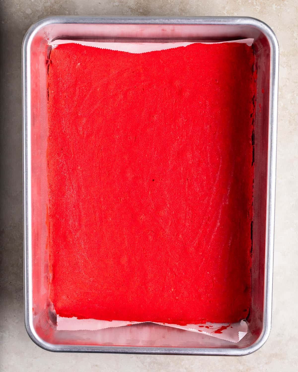 A baked rainbow cookie layer in a parchment-lined sheet pan.