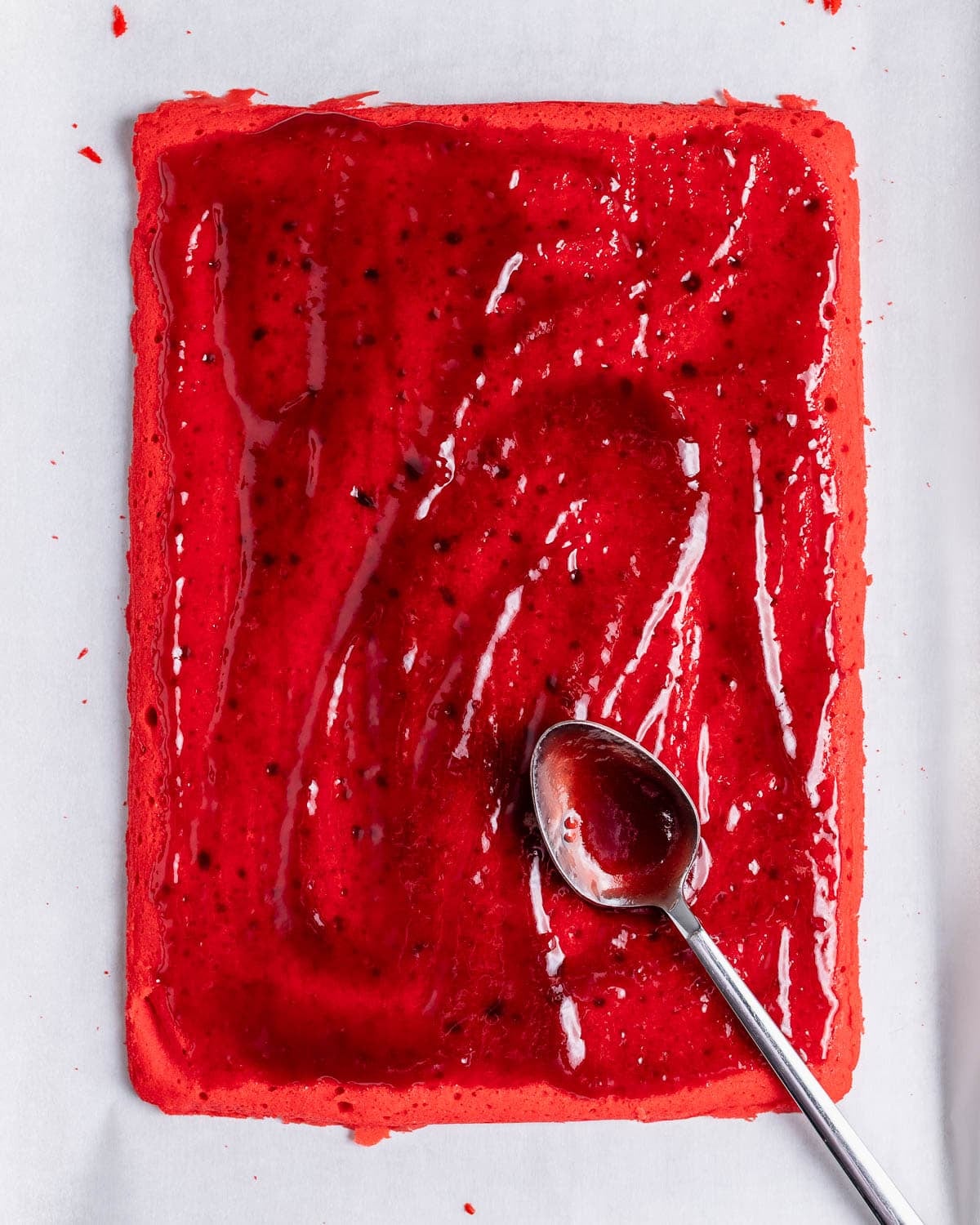 Raspberry jam being spread onto a baked layer of the rainbow cookies.