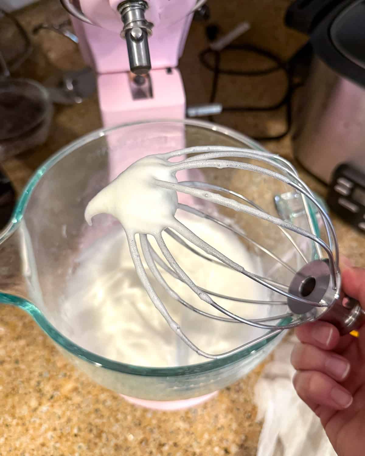 Soft peaks off the tip of a wire whisk attachment for a stand mixer.