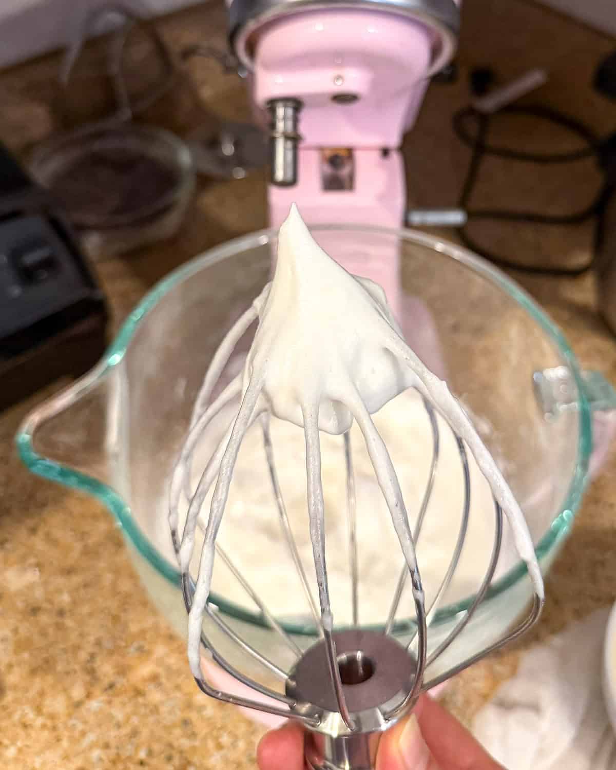 Stiff peaks standing up on a wire whisk attachment from a stand mixer.