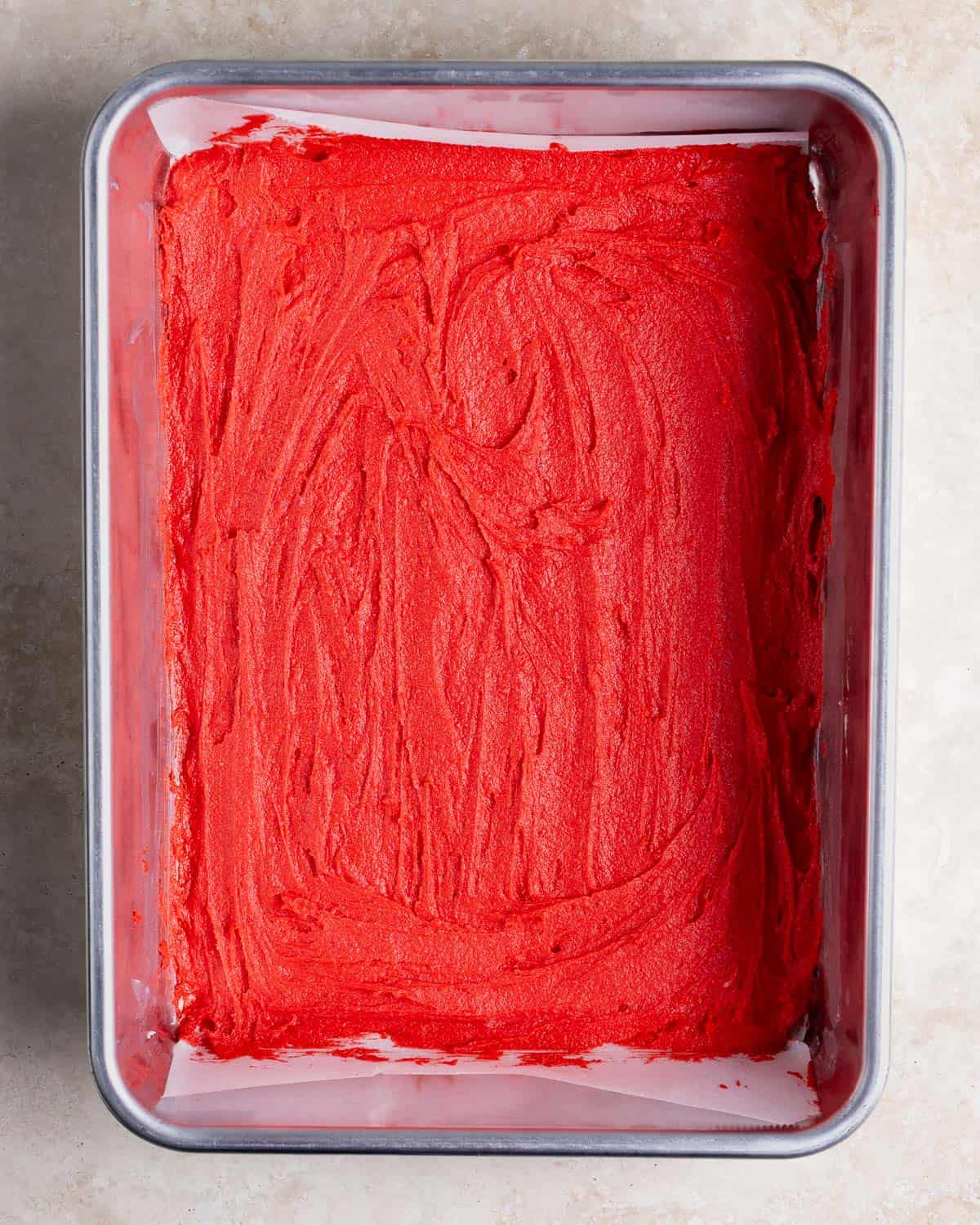 The red batter spread flat into a parchment-lined pan before baking.